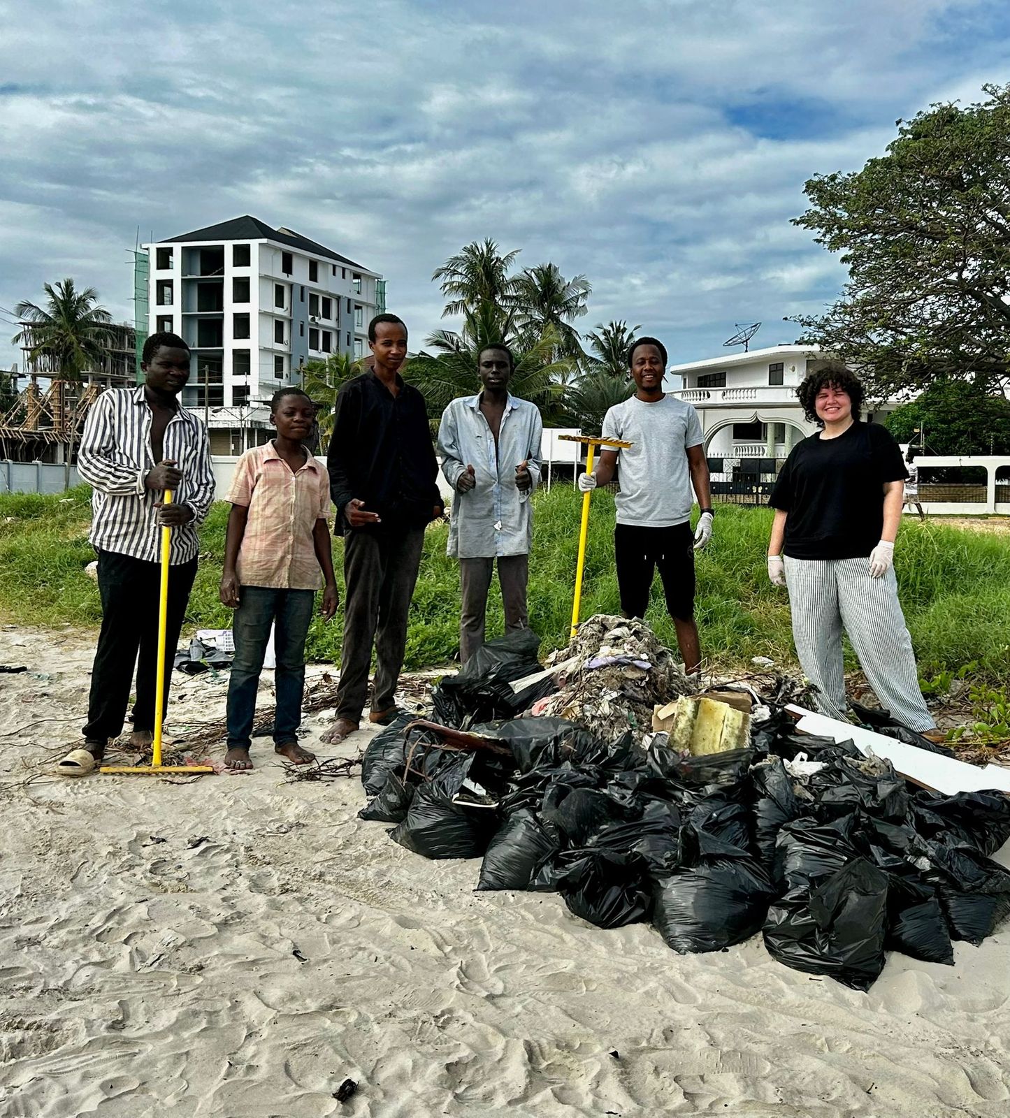 CoastClean Tanzania volunteers with bags of collected trash on the beach in Dar es Salaam